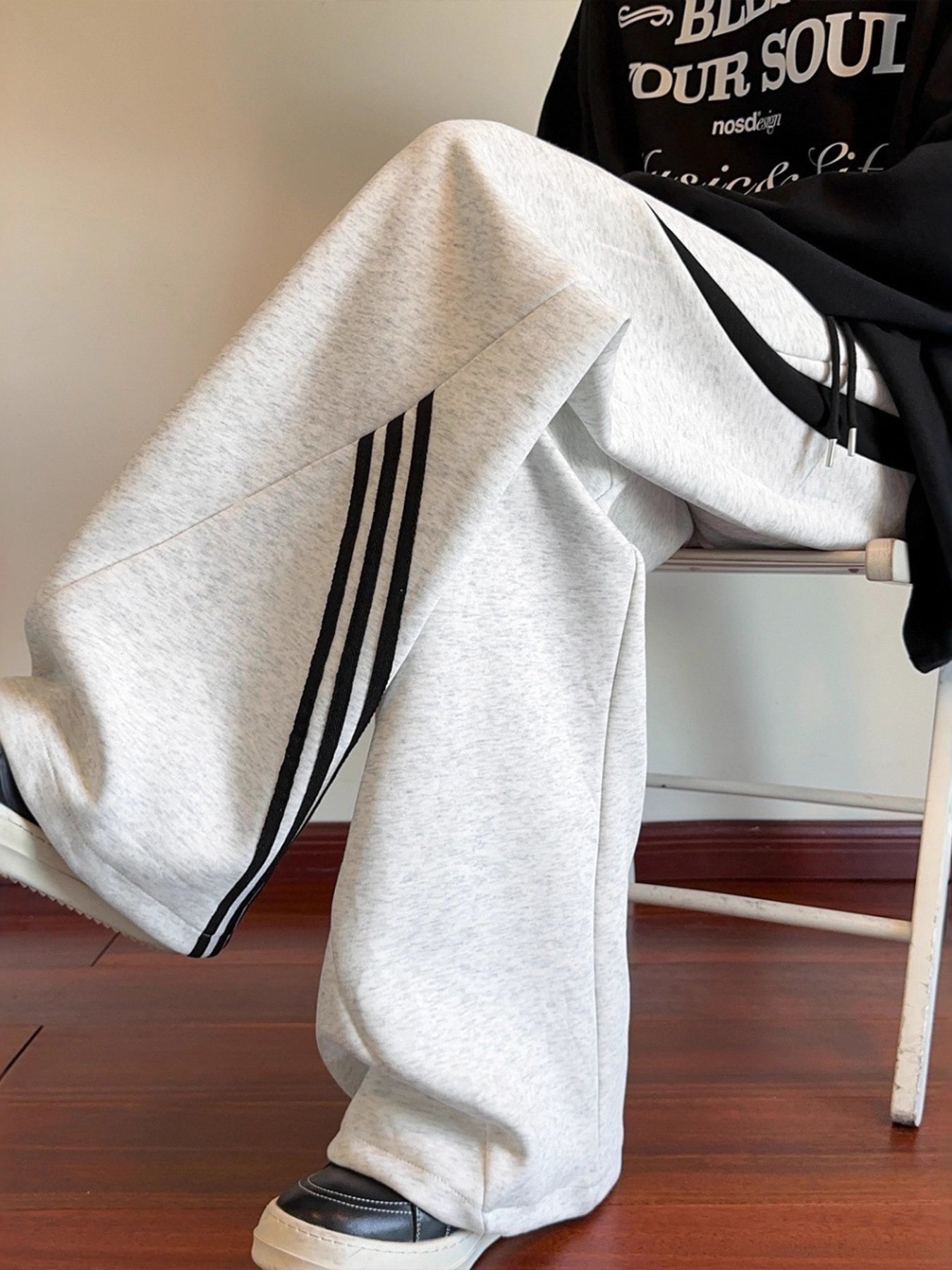 Model sitting in the Concrete Grey Arc Silhouette sweatpants, showcasing the high-contrast black stripes and the premium drape of the tech-blend fabric.