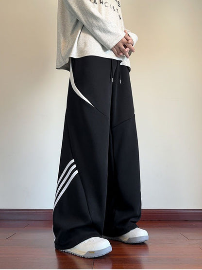 Side-angle shot of the UU Arc Silhouette sweatpants in Midnight Black, showing the oversized fit and the white curved stripe detail.