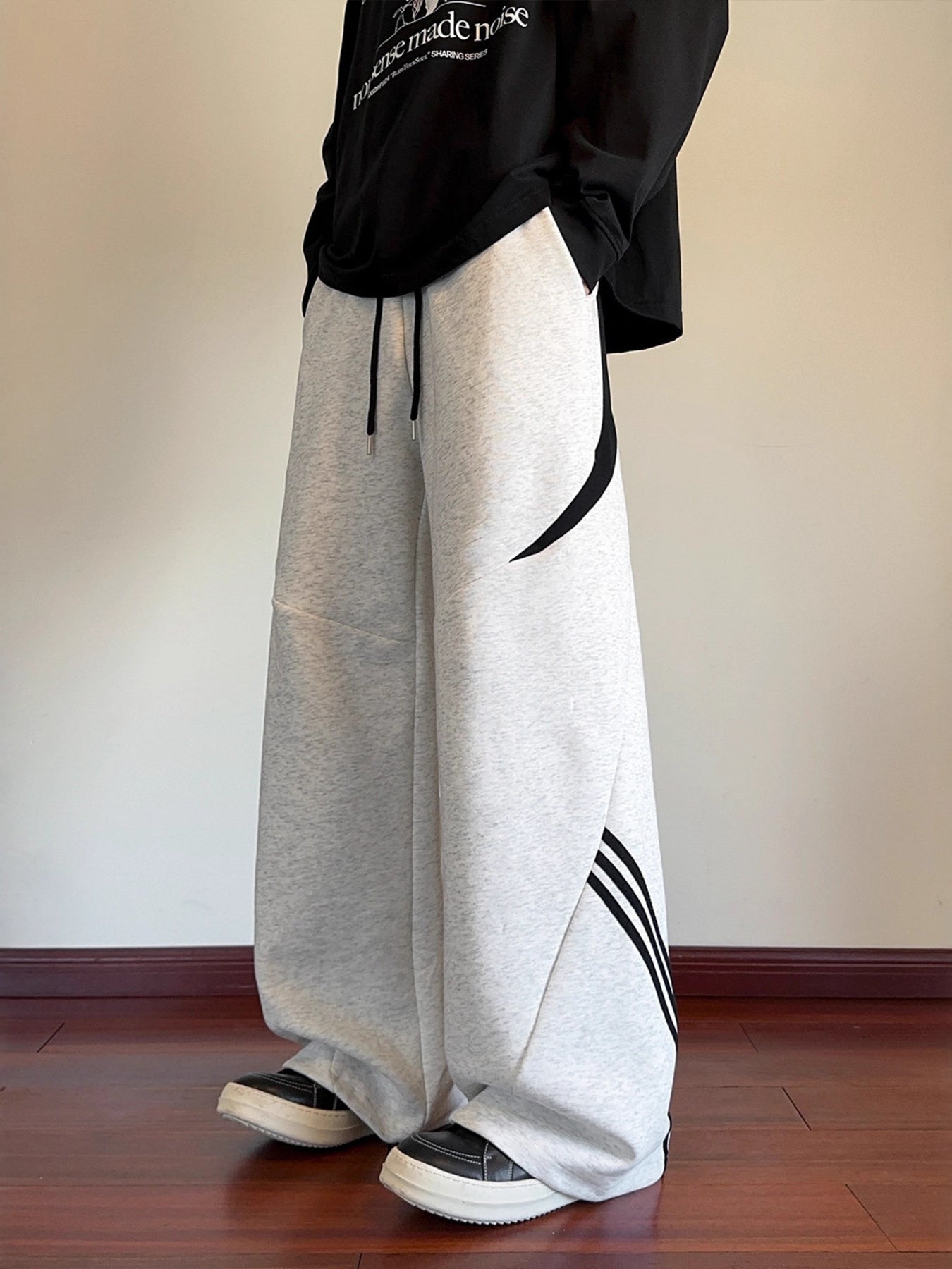Front-side view of the UU Arc Silhouette sweatpants in Concrete Grey, highlighting the black asymmetrical arc design and wide-leg drape.