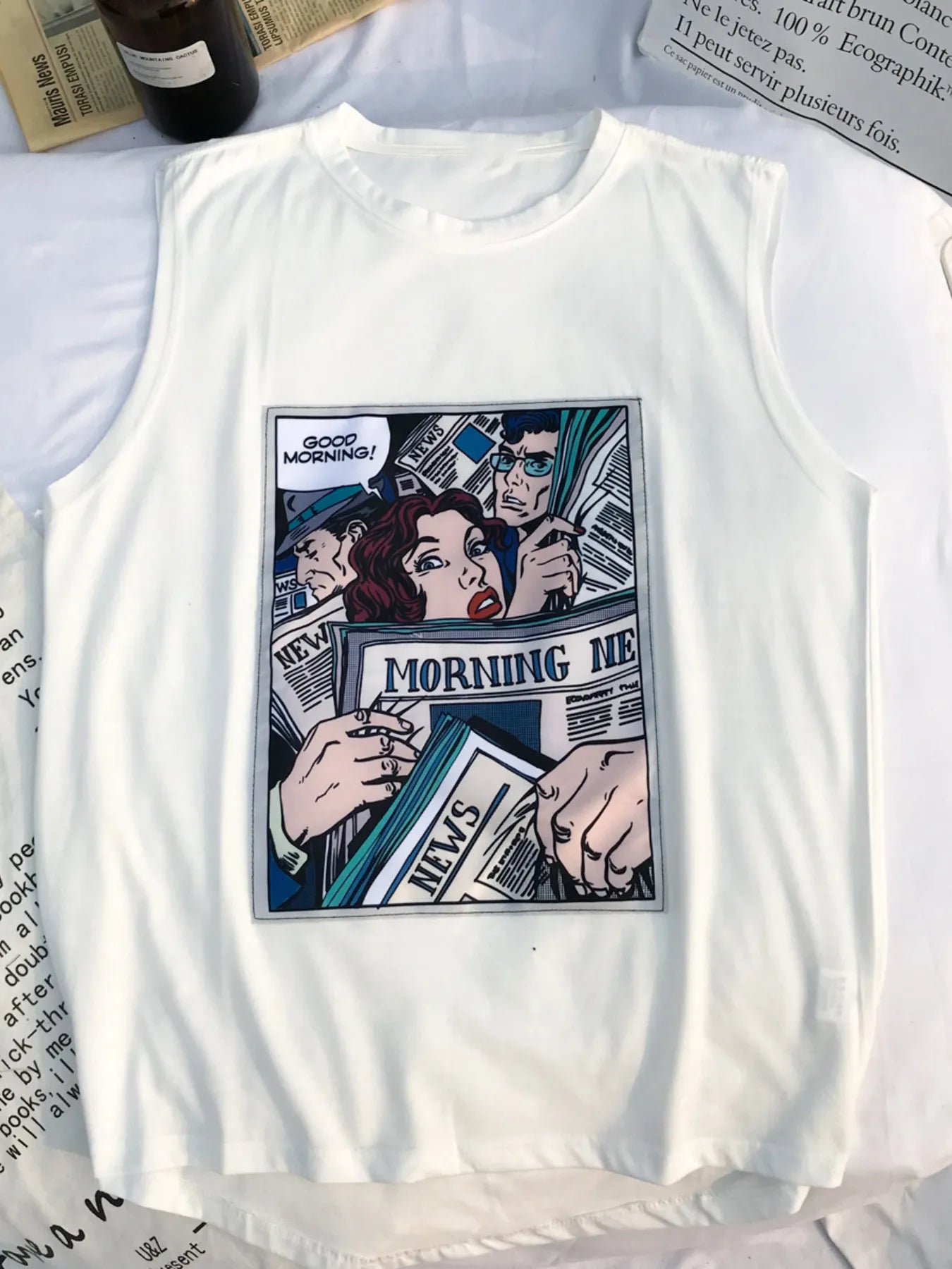 URBAN UNIT Morning News Graphic Tank in Raw White. Flat lay view showing the retro comic print on a sleeveless streetwear shirt.