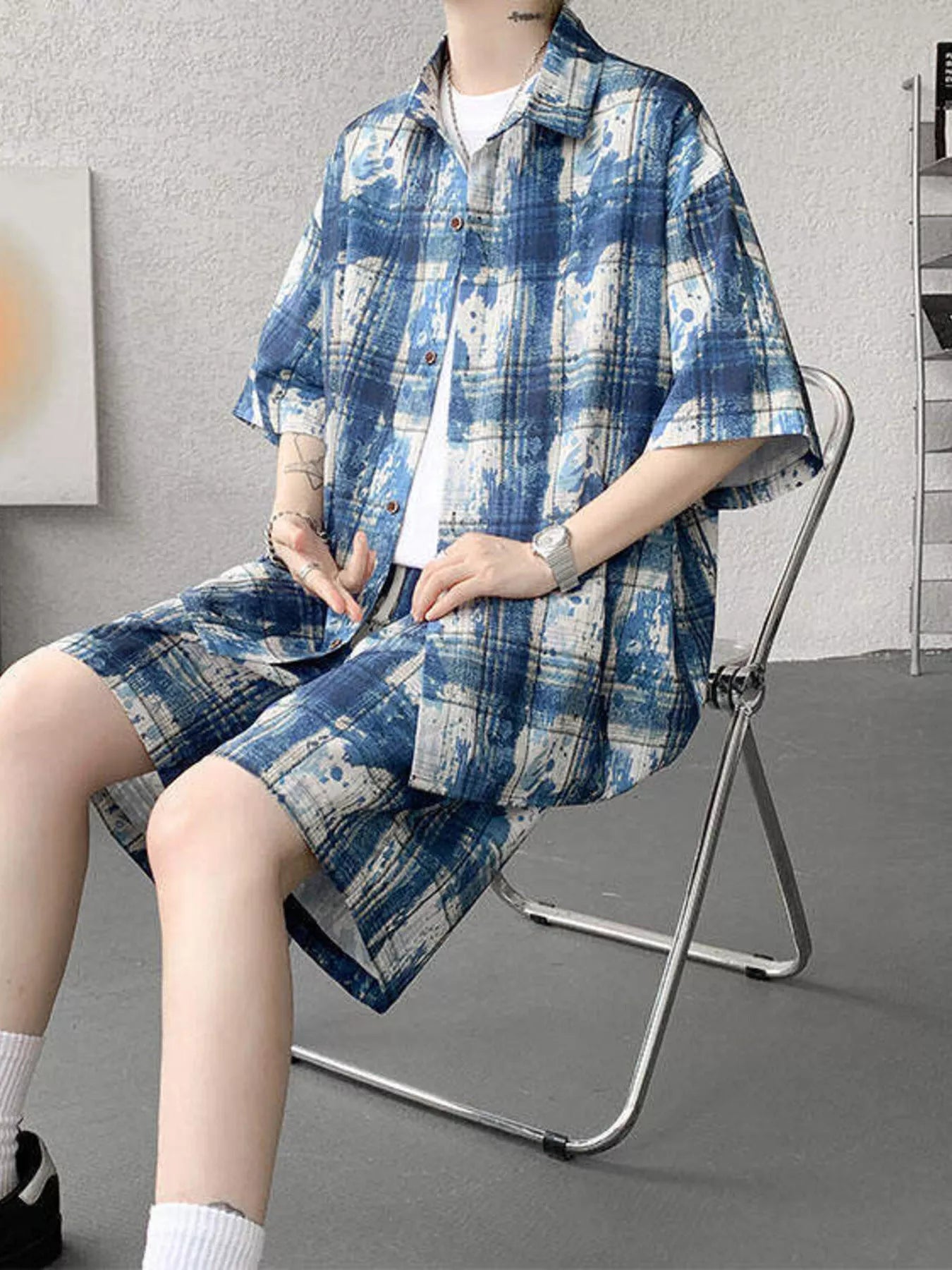 Model sitting on a metal chair wearing the URBAN UNIT OFF-GRID Plaid Set in Electric Blueprint, demonstrating the freedom of movement and wide-leg shorts.