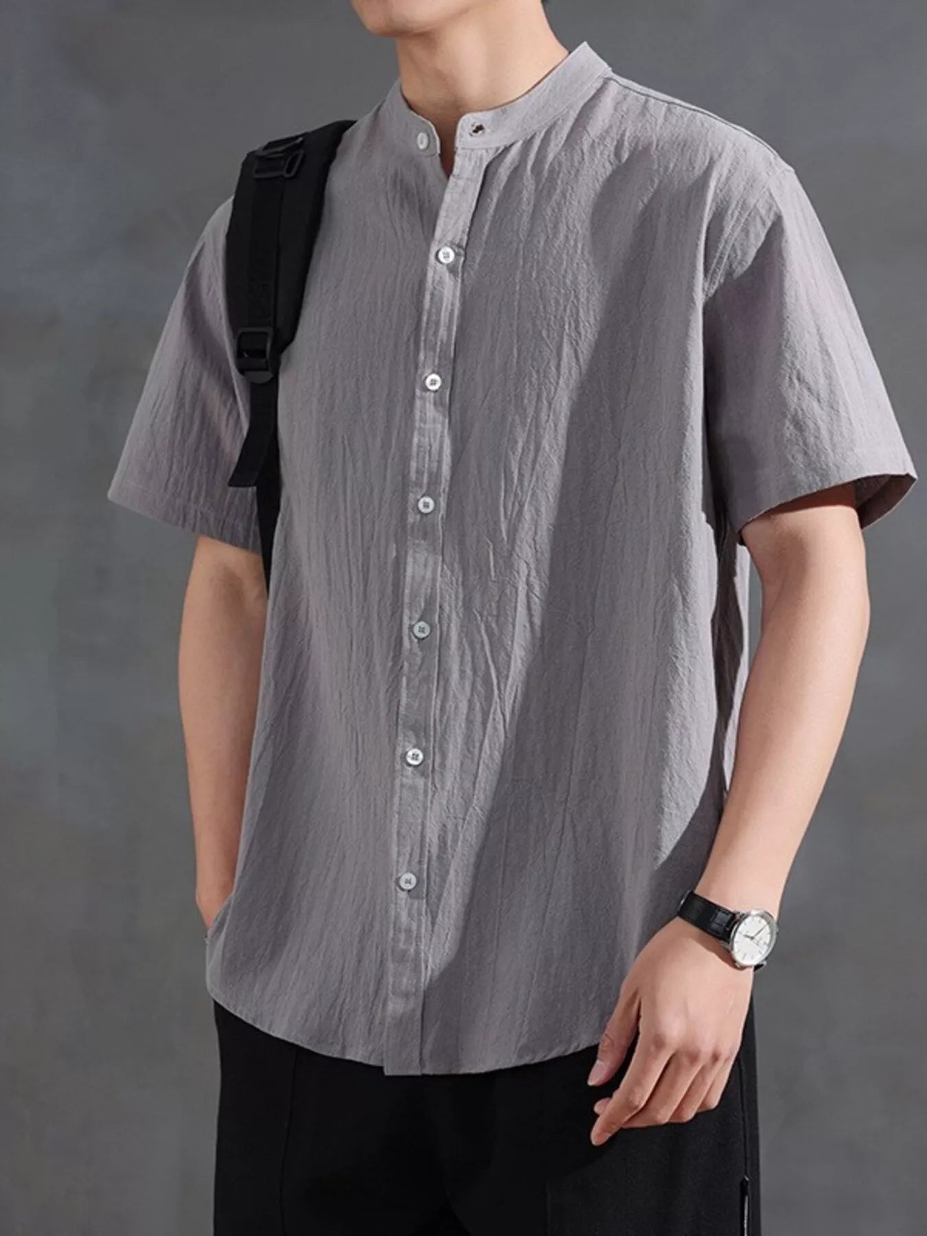 Model wearing the URBAN UNIT Origin Silhouette Mandarin Collar Shirt in Asphalt Grey, styled with a black backpack. Raw, industrial streetwear essential for the city.